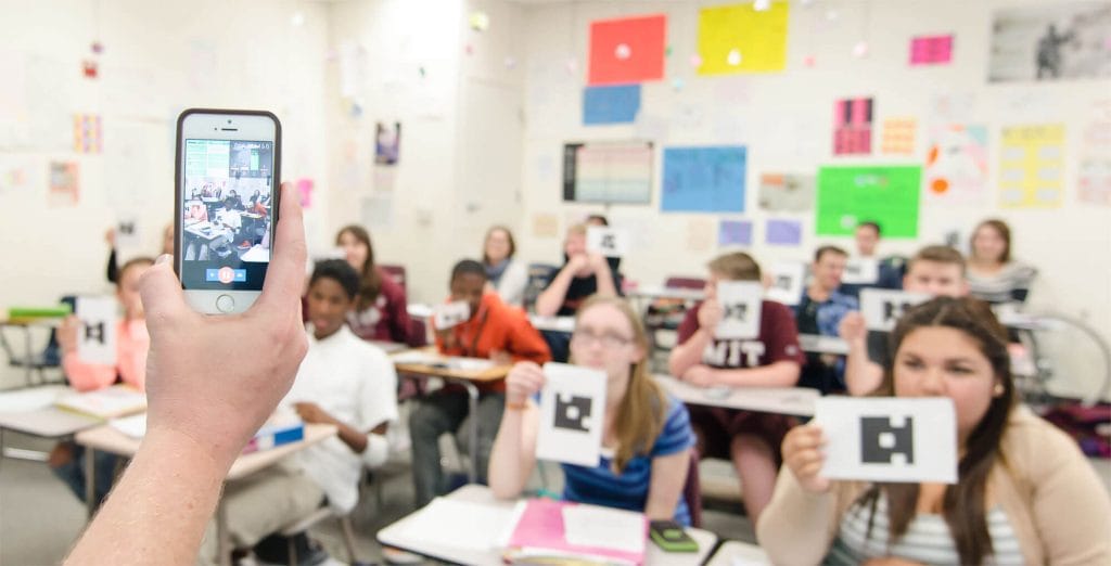 A classroom of students using the Plickers app with their teacher