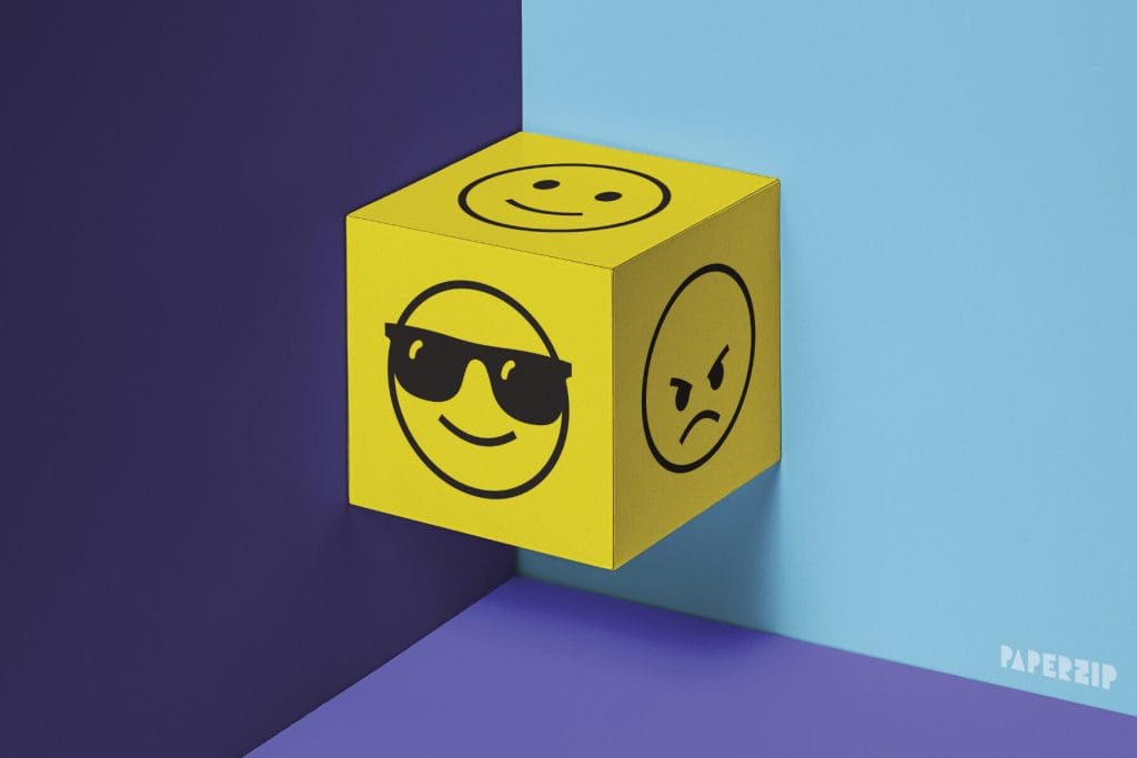 A yellow emoji dice made out of paper displaying emoji expressions. The background is purple and blue.